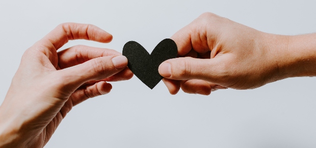 two hands holding a black paper heart