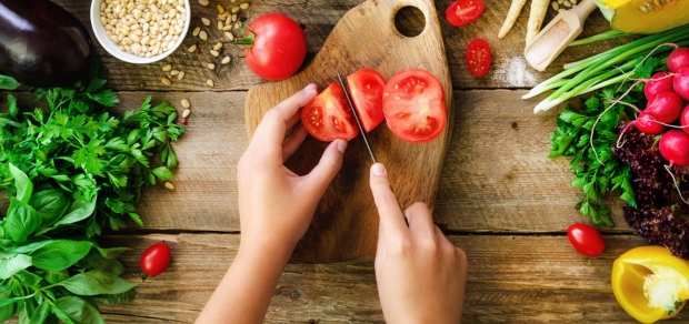 tomato being chopped on a cutting board with other vegetables surrounding it